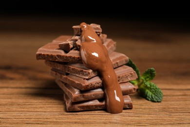 Photo of Pieces of milk chocolate with tasty paste and mint on wooden table, closeup
