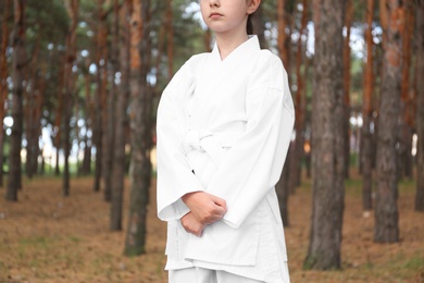 Photo of Cute little girl in kimono practicing karate in forest, closeup