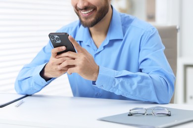 Man using smartphone at white table in office, closeup