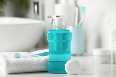 Mouthwash, toothbrush, towel and dental floss on white countertop in bathroom