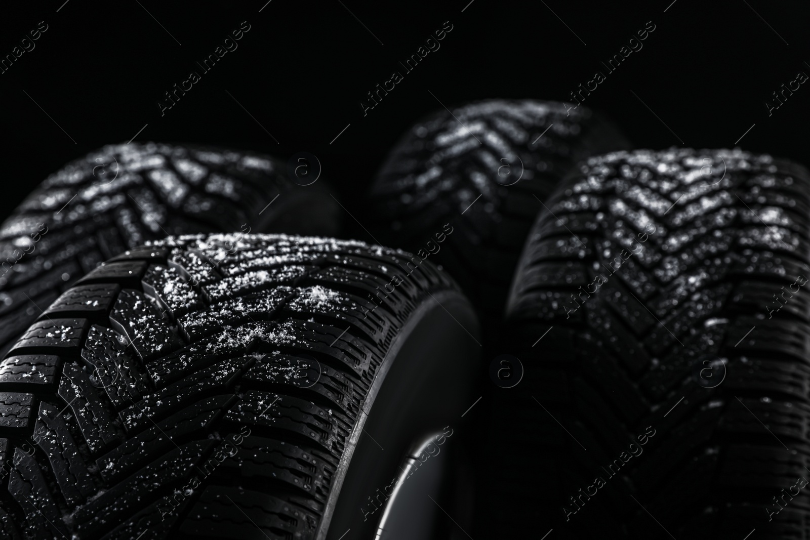Photo of Snowy set of wheels with winter tires on black background, closeup. Space for text