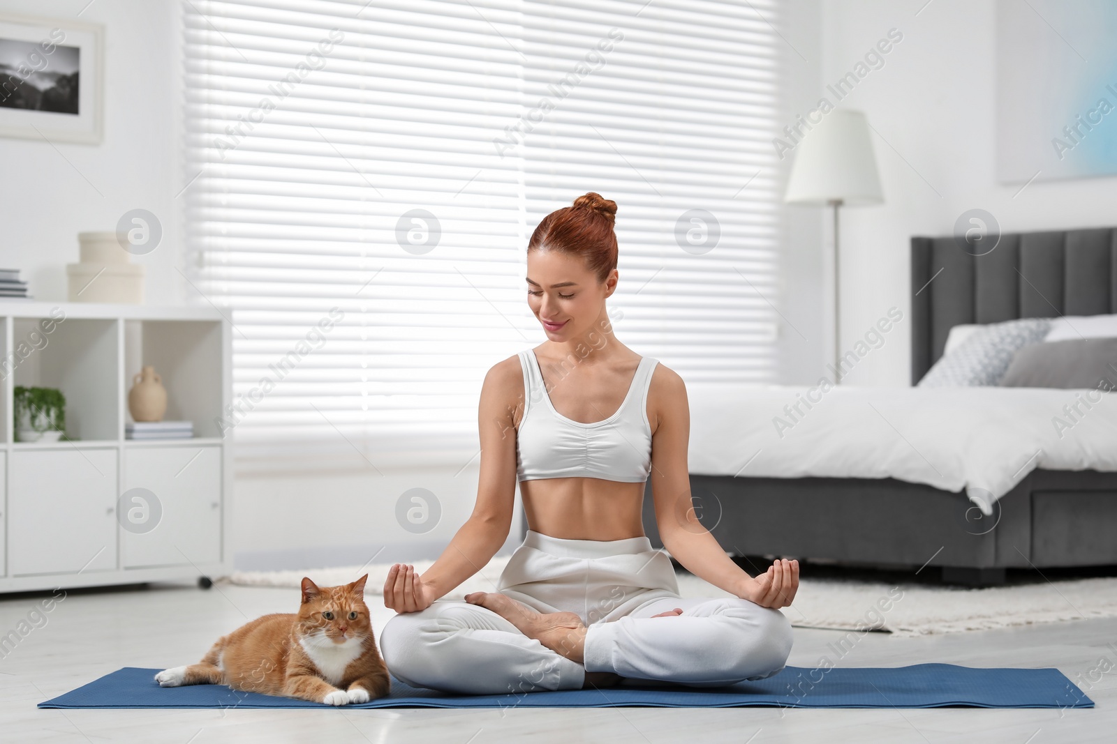 Photo of Beautiful woman with cute red cat practicing yoga on mat at home