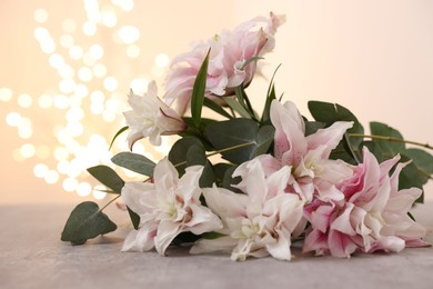 Photo of Bouquet of beautiful lily flowers on table against beige background with blurred lights, closeup