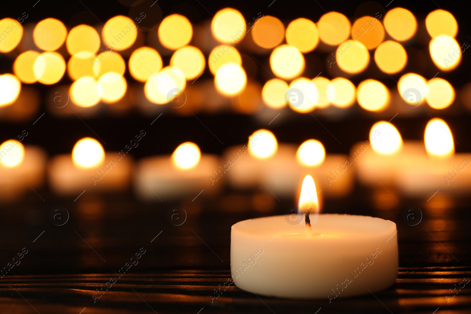 Photo of Burning candle on black table against blurred background, space for text