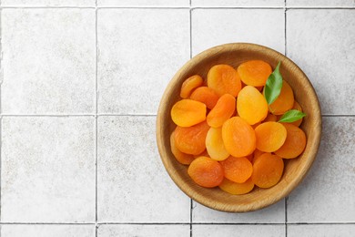 Wooden bowl of tasty apricots and space for text on white tiled table, top view. Dried fruits