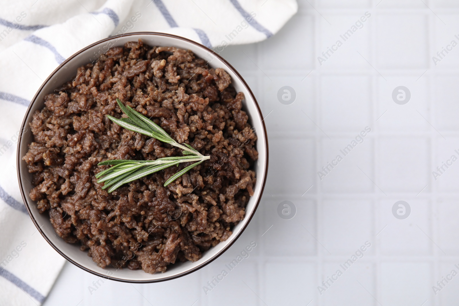 Photo of Fried ground meat in bowl and rosemary on white tiled table, top view. Space for text