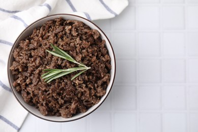 Fried ground meat in bowl and rosemary on white tiled table, top view. Space for text