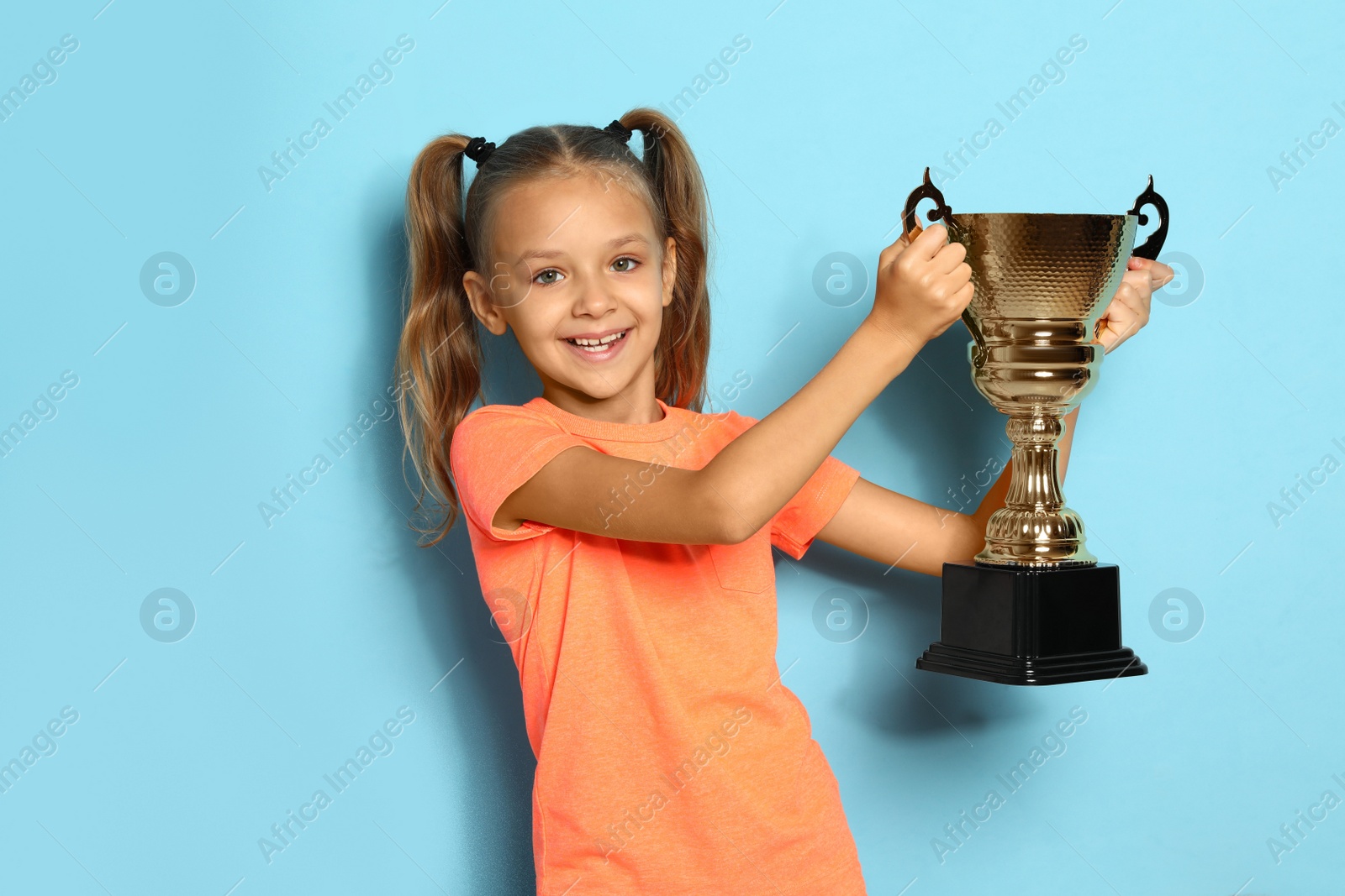 Photo of Happy girl with golden winning cup on blue background