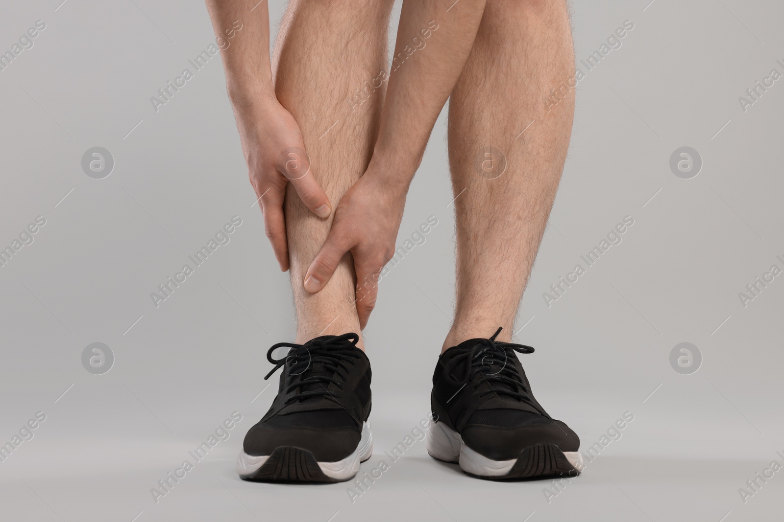 Photo of Man suffering from leg pain on grey background, closeup