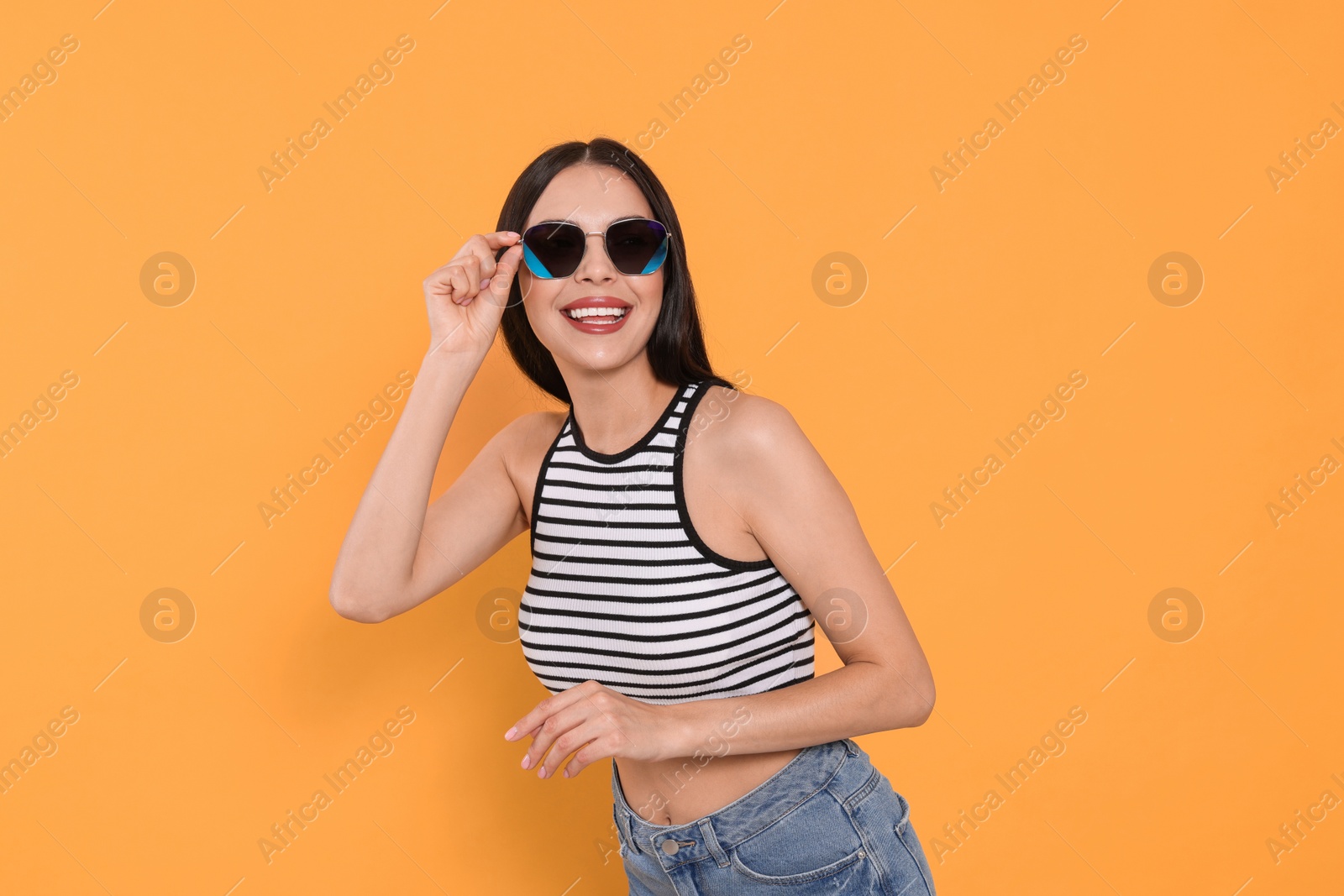 Photo of Attractive happy woman touching fashionable sunglasses against orange background