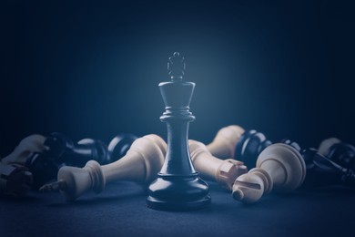 Image of Black king among fallen chess pieces on black background, dark blue toned
