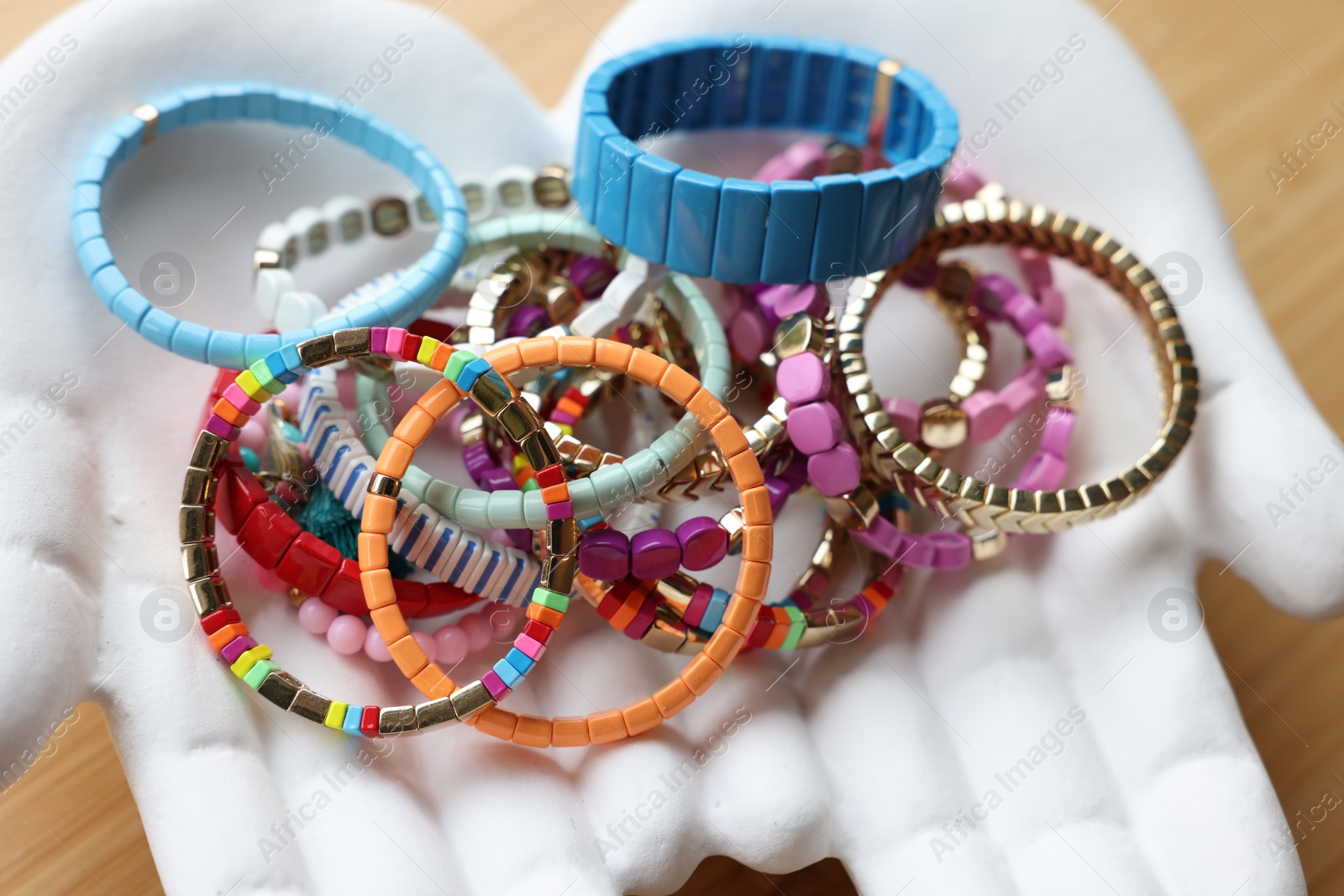 Photo of Ceramic hand stand with many stylish bracelets on wooden table, closeup