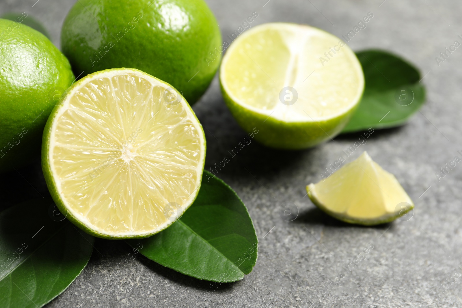 Photo of Fresh ripe limes and leaves on grey table, closeup