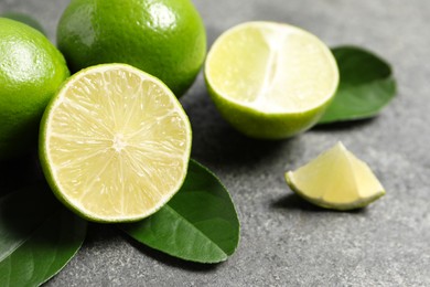 Fresh ripe limes and leaves on grey table, closeup