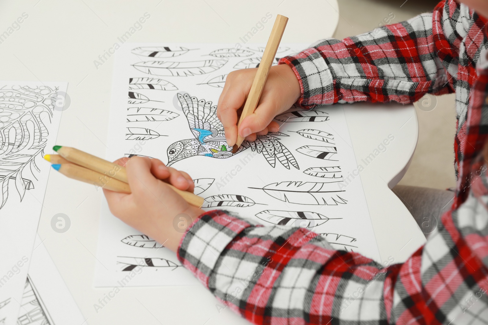 Photo of Little girl coloring antistress page at table, closeup