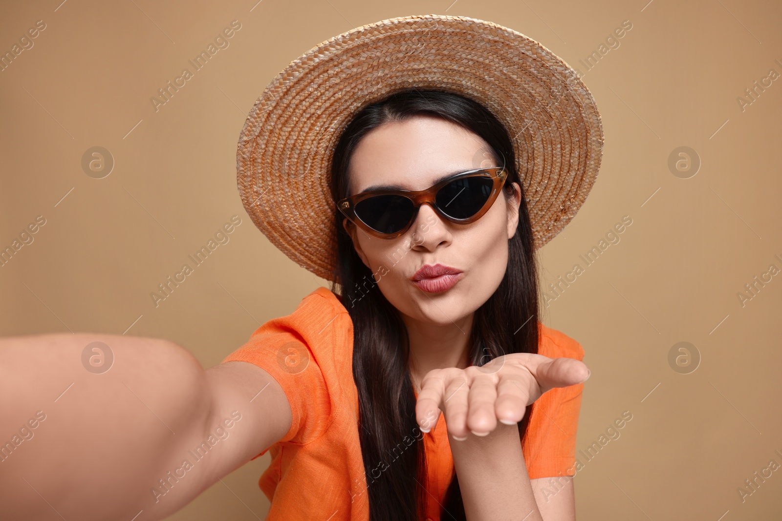 Photo of Beautiful young woman in straw hat taking selfie while blowing kiss on beige background, closeup