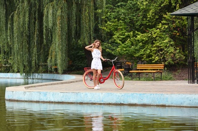 Beautiful woman in casual outfit with bicycle near pond outdoors