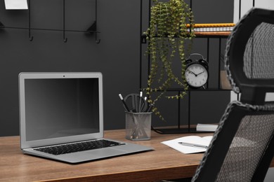 Photo of Cozy workplace with modern laptop on desk and comfortable chair at home