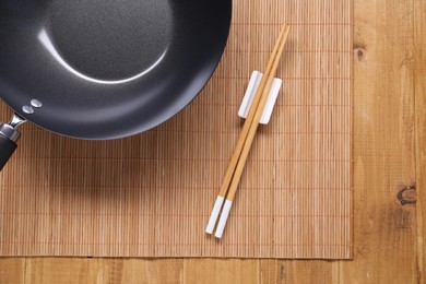 Empty iron wok and chopsticks on wooden table, top view