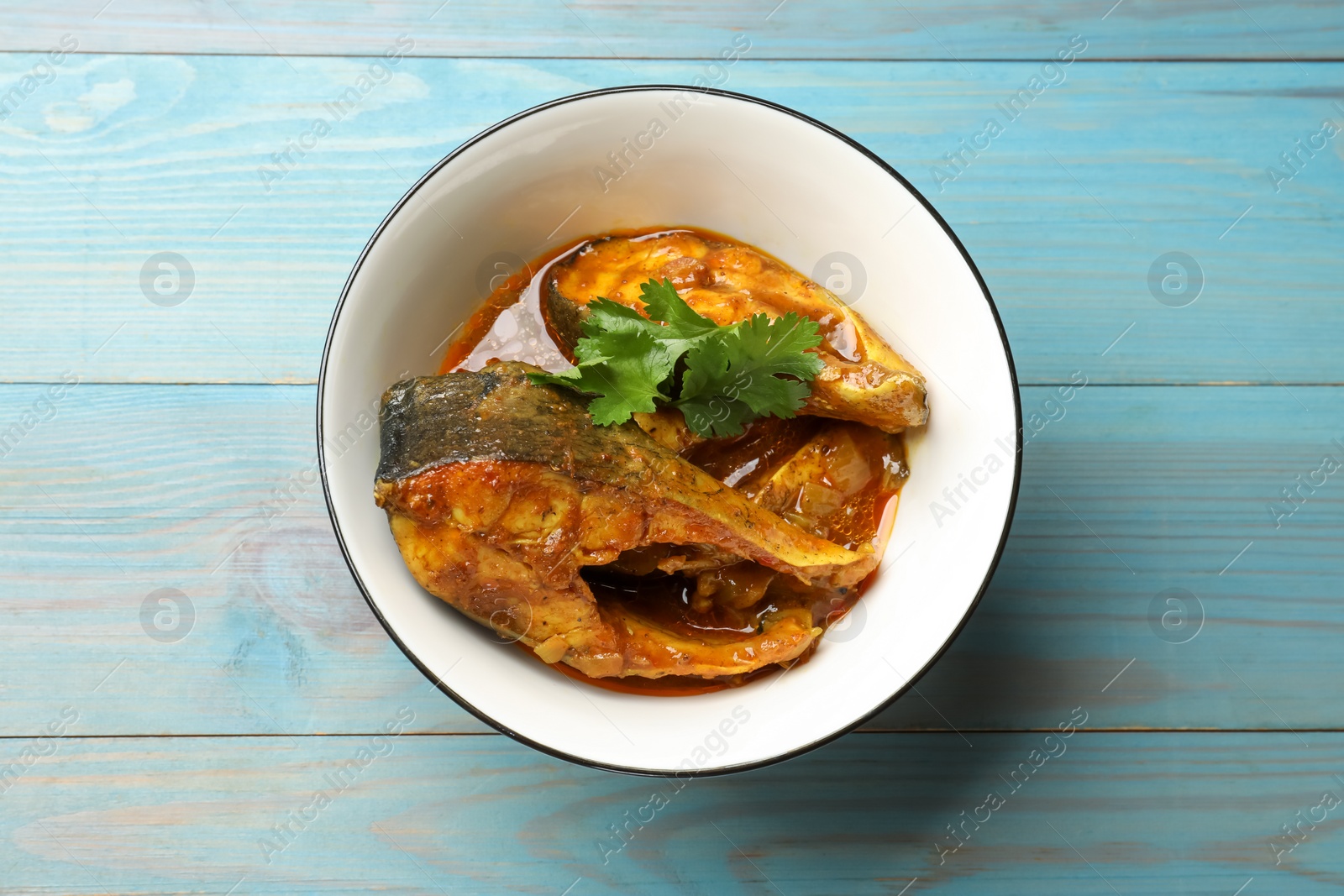 Photo of Tasty fish curry on light blue wooden table, top view. Indian cuisine