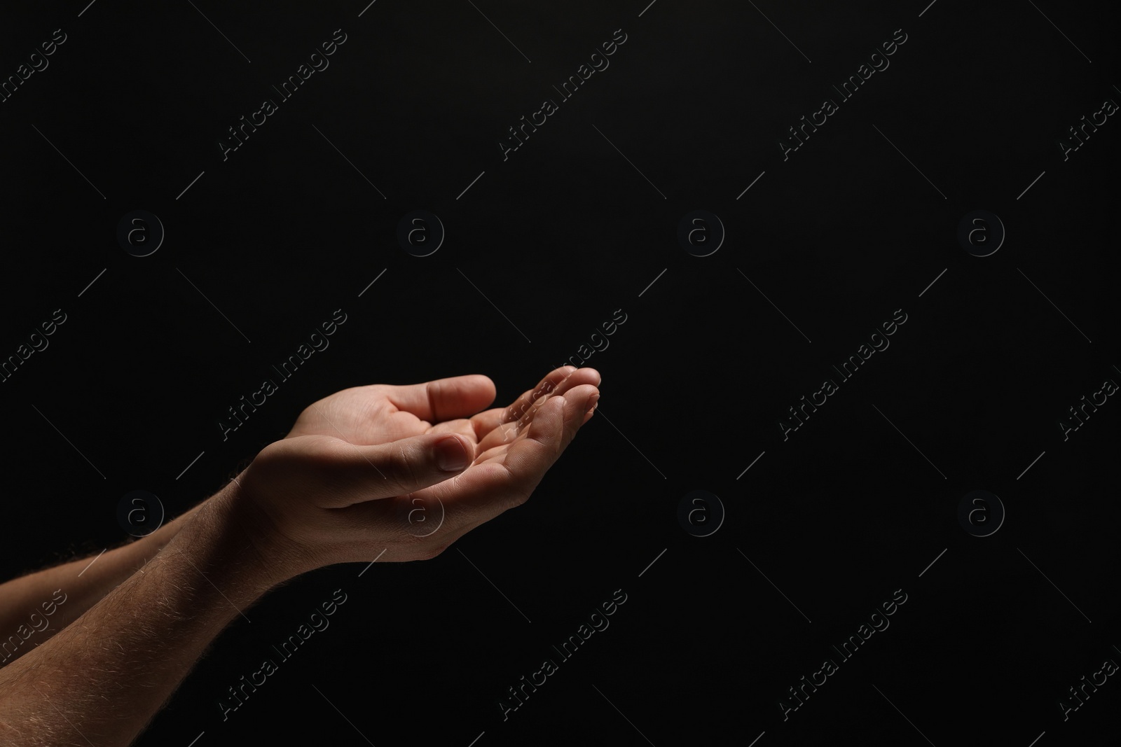 Photo of Religion. Man with open palms praying on black background, closeup. Space for text