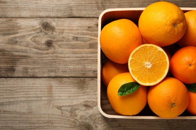 Photo of Many whole and cut ripe oranges on wooden table, top view. Space for text