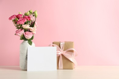 Happy Mother's Day. Gift box, blank card and bouquet of beautiful flowers in vase on white table against pink background. Space for text