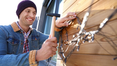 Photo of Man decorating house with Christmas lights outdoors