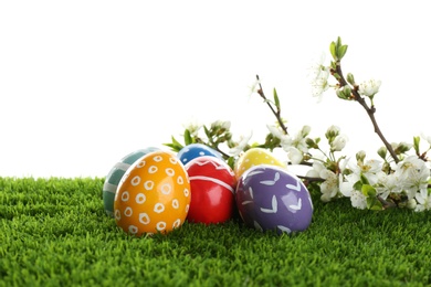 Photo of Painted Easter eggs and blossoming branches on green grass against white background