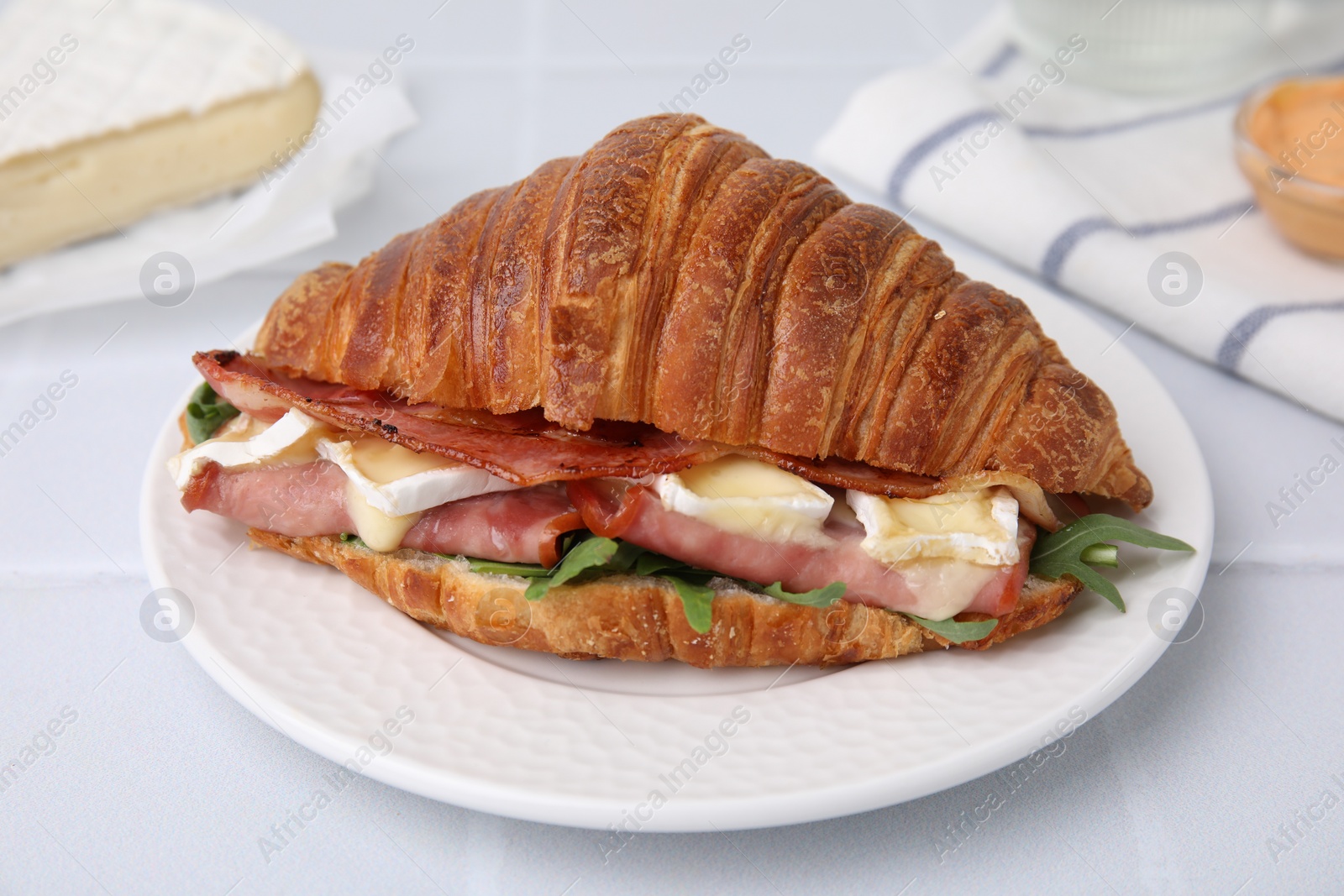 Photo of Tasty croissant with brie cheese, ham and bacon on white table, closeup