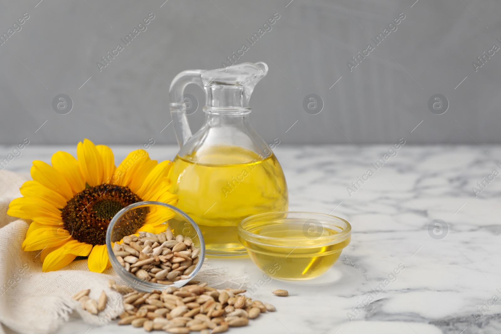 Photo of Sunflower, oil and seeds on white marble table, space for text