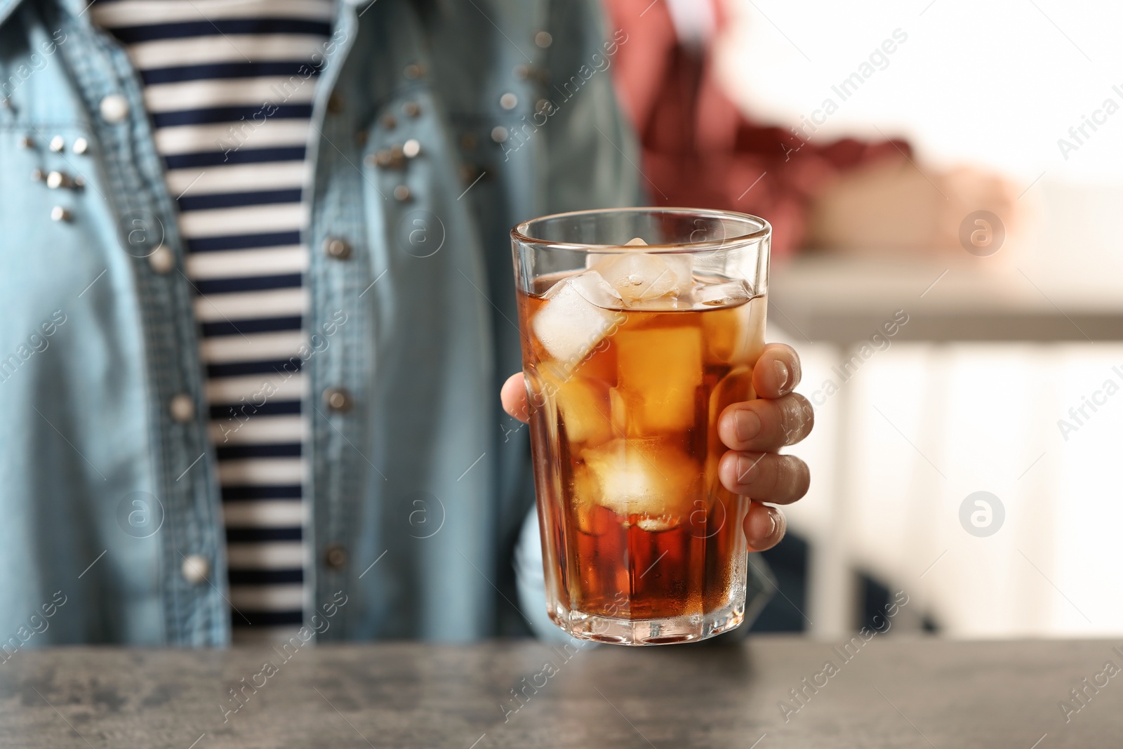 Photo of Woman holding glass of cola with ice at table, closeup