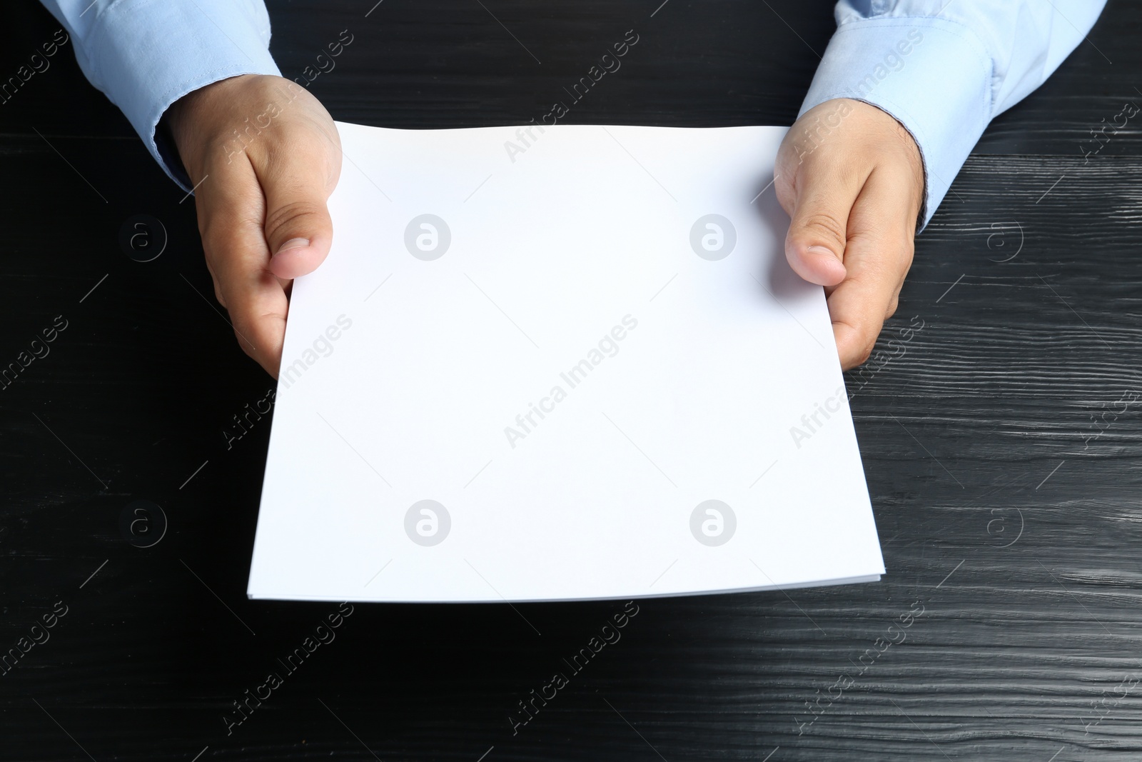 Photo of Man holding blank paper sheets for brochure at black wooden table. Mock up