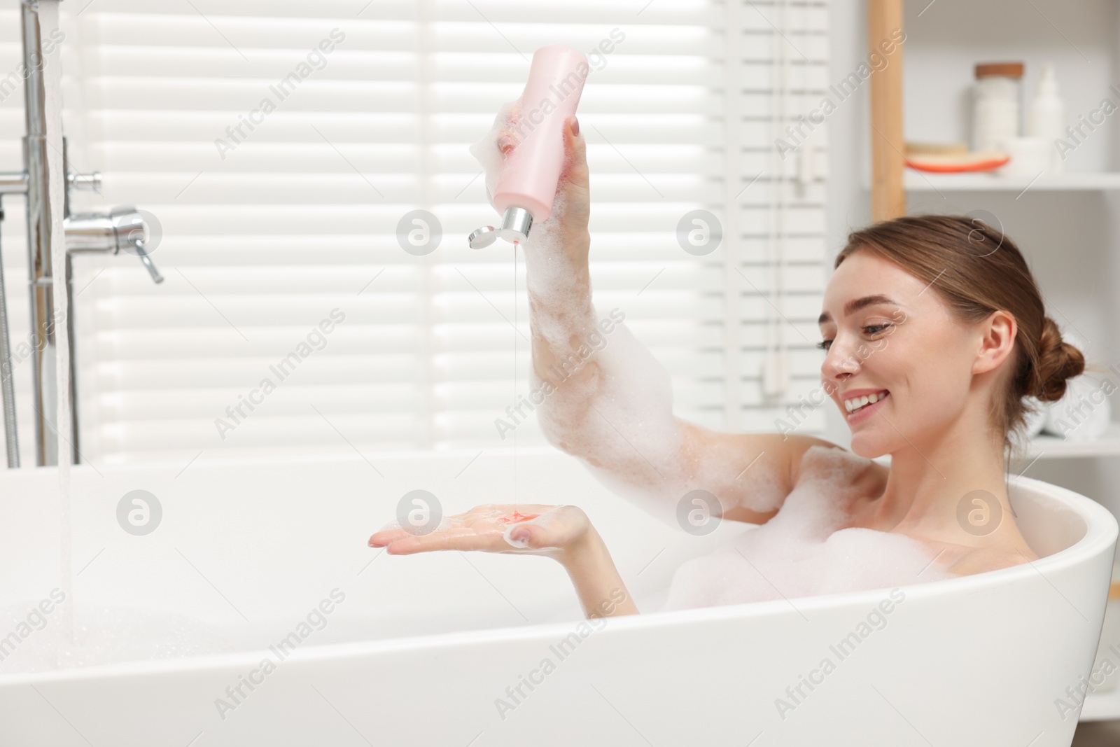 Photo of Woman pouring shower gel onto hand in bath indoors