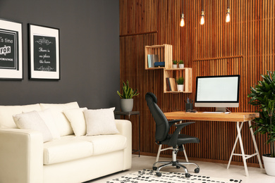 Comfortable workplace with computer near wooden wall in stylish room interior. Home office design