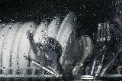 Photo of Clean plates and cutlery in dishwasher, view through wet glass