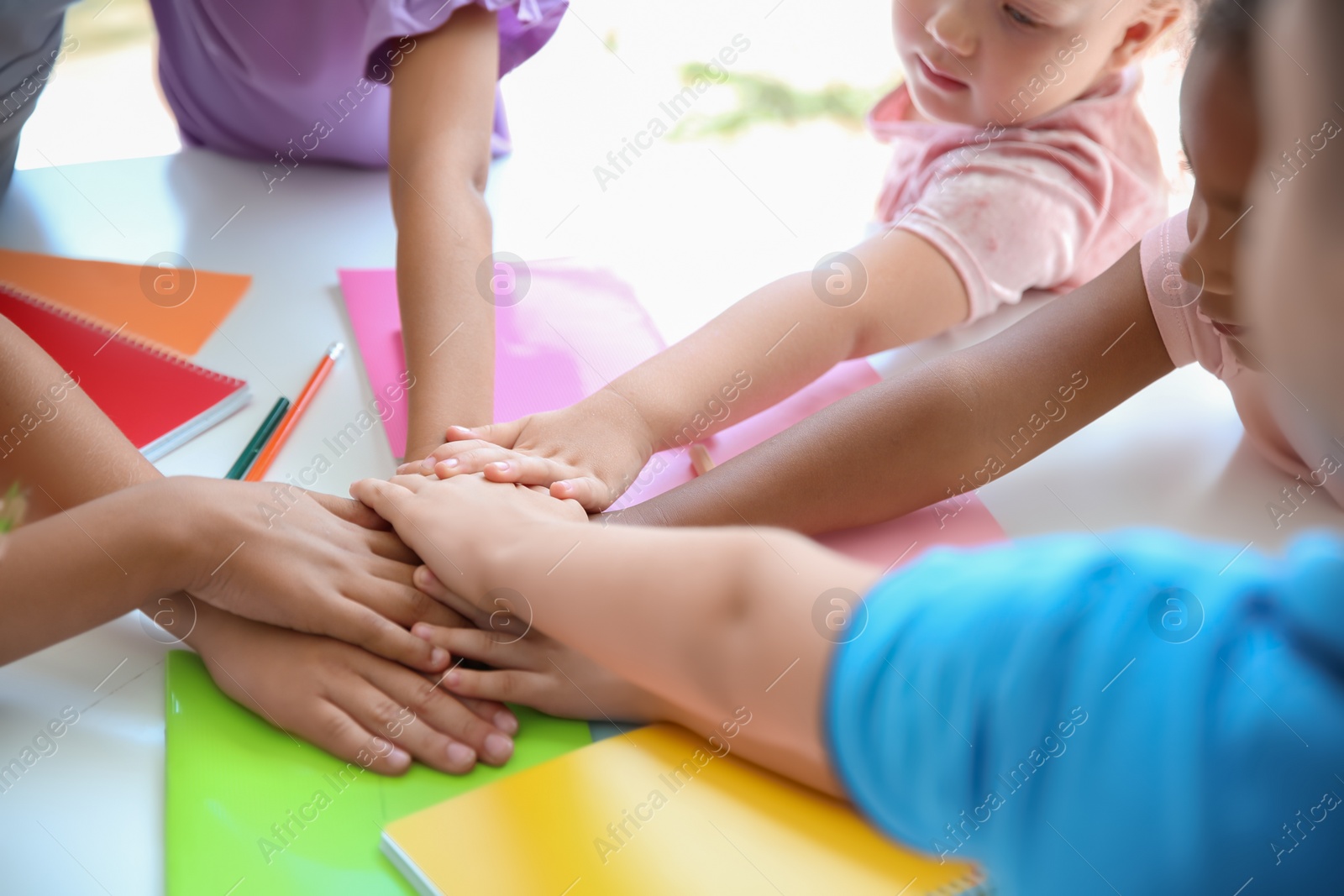 Photo of Little children putting their hands together at table, closeup. Unity concept