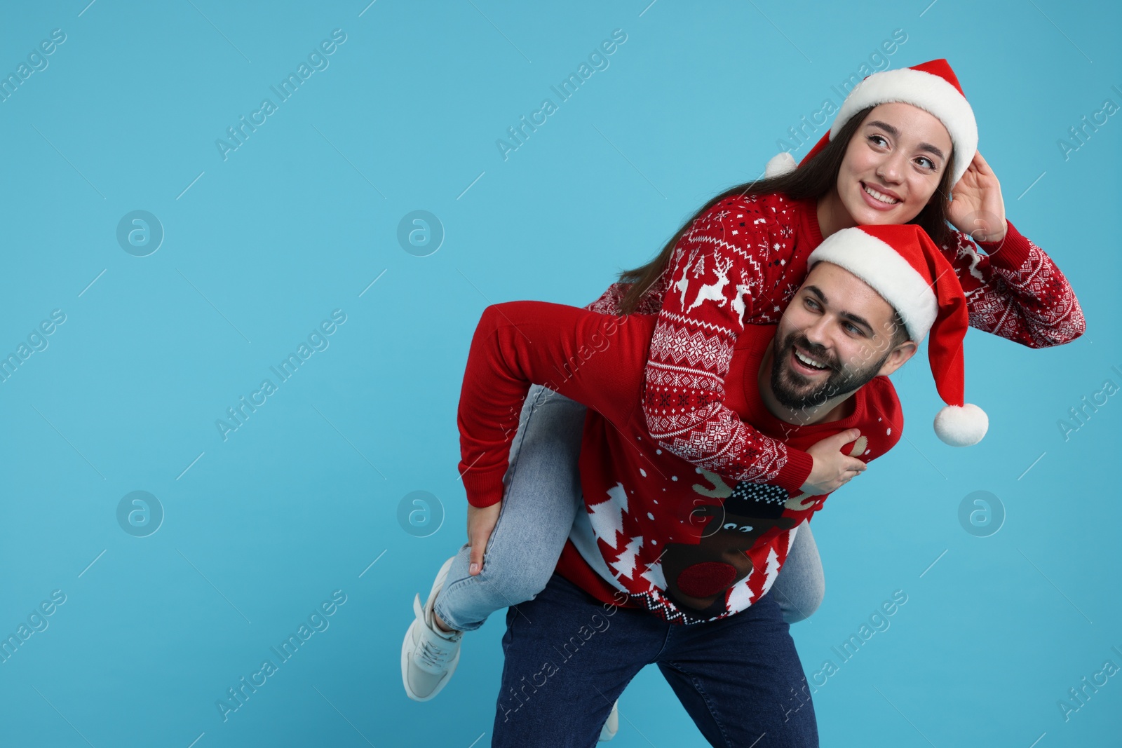 Photo of Happy young couple in Christmas sweaters and Santa hats on light blue background. Space for text