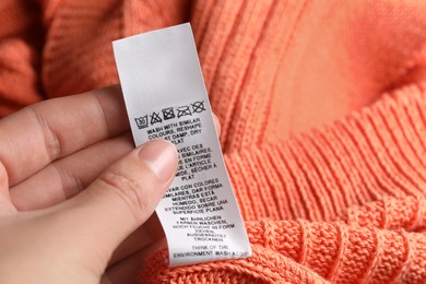 Photo of Woman holding clothing label on orange garment, closeup