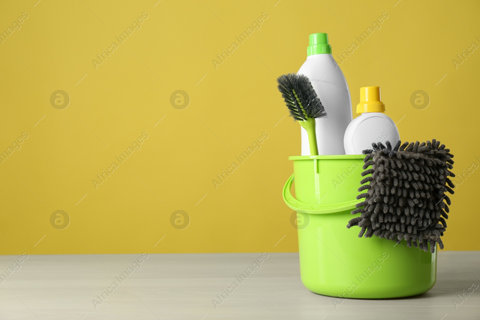 Photo of Bucket with cleaning products and tools on grey table. Space for text