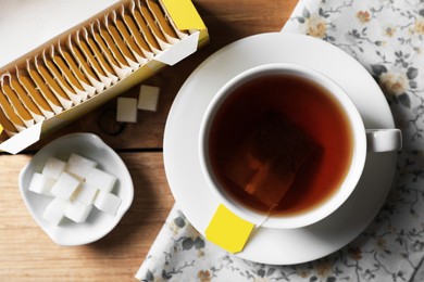 Photo of Tea bags package, sugar and cup of hot drink on wooden table, flat lay