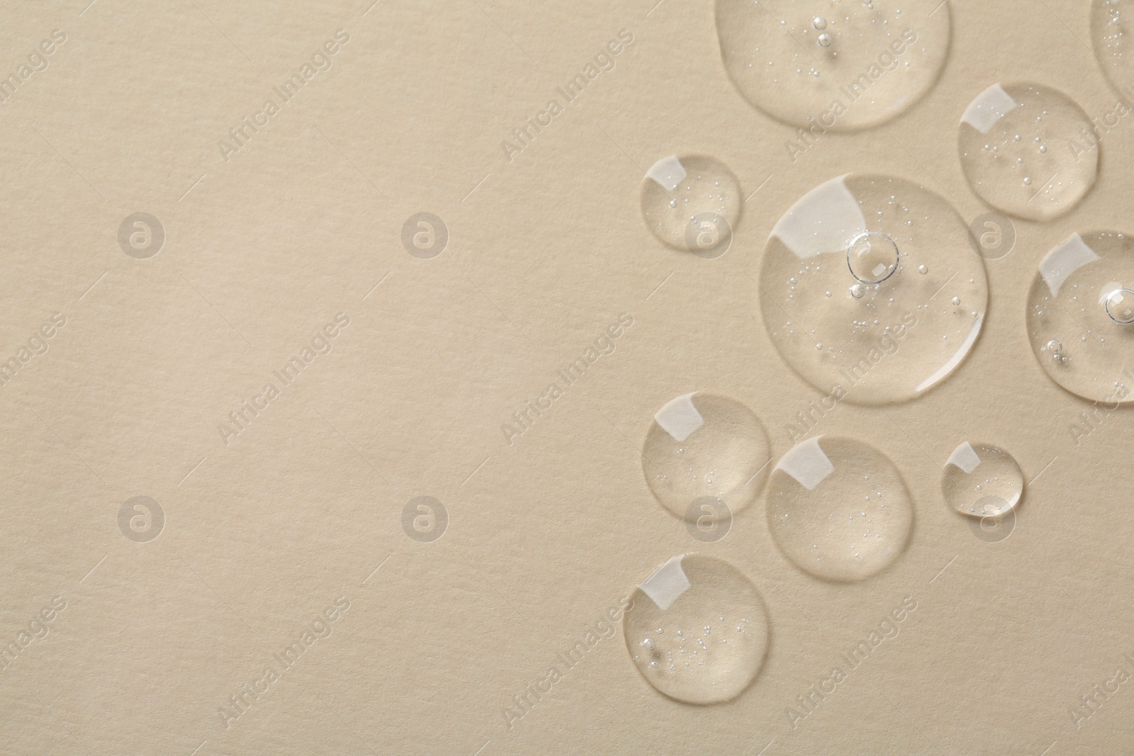 Photo of Drops of cosmetic serum on beige background, top view. Space for text