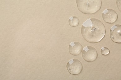 Photo of Drops of cosmetic serum on beige background, top view. Space for text
