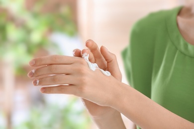 Photo of Young woman applying cream on her hands indoors, closeup