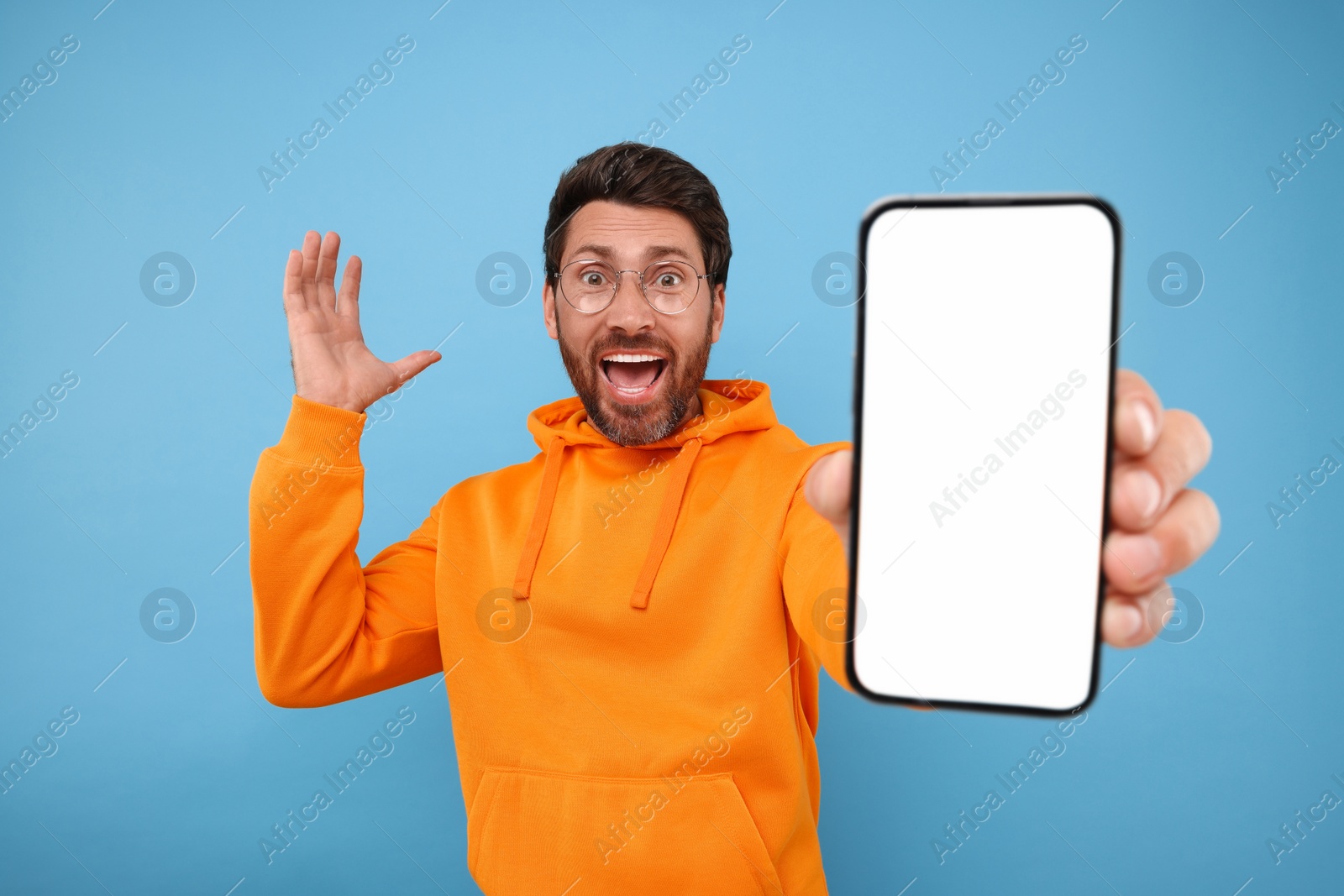 Photo of Surprised man showing smartphone in hand on light blue background