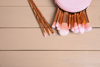 Set of professional makeup brushes with bag on wooden background, above view. Space for text