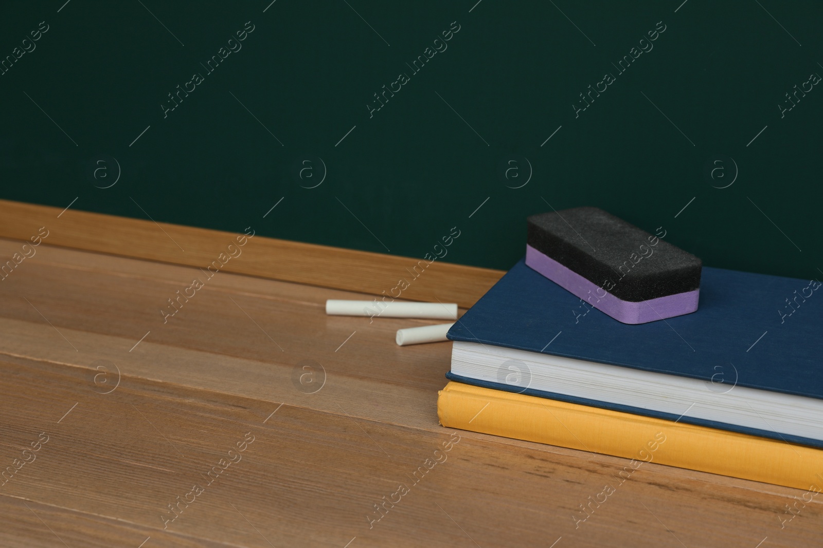 Photo of Books, pieces of chalk and duster on wooden table near greenboard, space for text