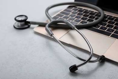Photo of Laptop with stethoscope on white table, closeup. Space for text