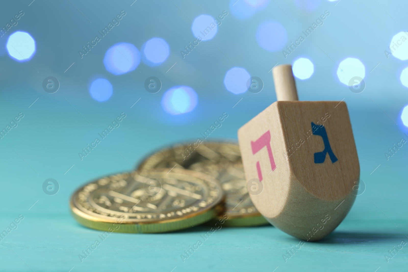 Photo of Hanukkah celebration. Wooden dreidel with jewish letters and coins against light blue background with blurred lights. Space for text