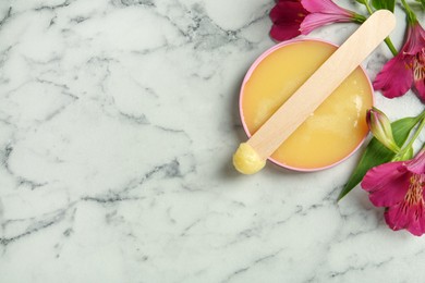 Spatula with wax and flowers on white marble table, flat lay. Space for text